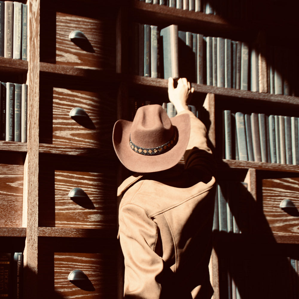 Person wearing a fedora hat beside a bookshelf