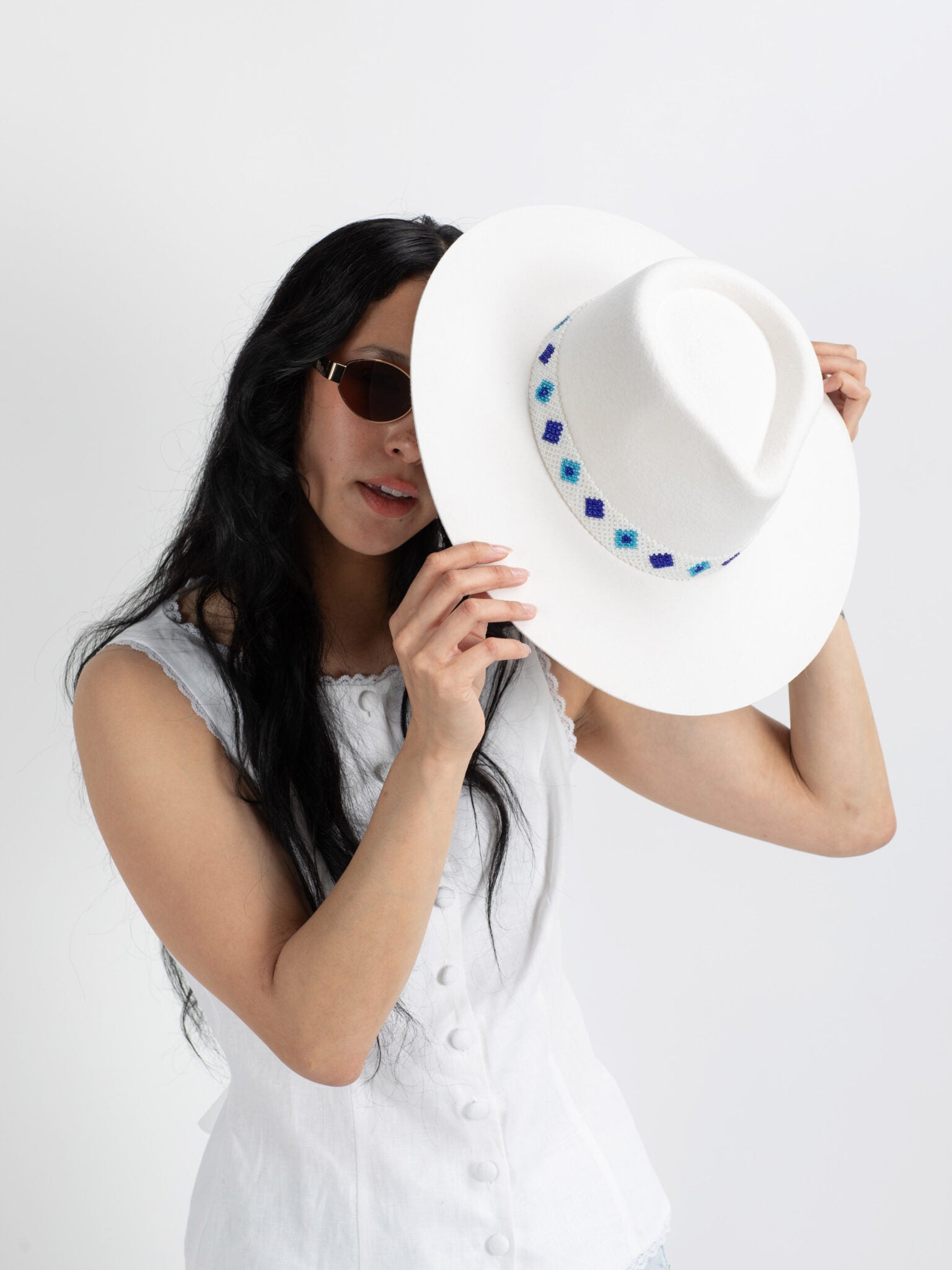 Woman holding a white Santorini handmade fedora hat with decorative elements against a plain background