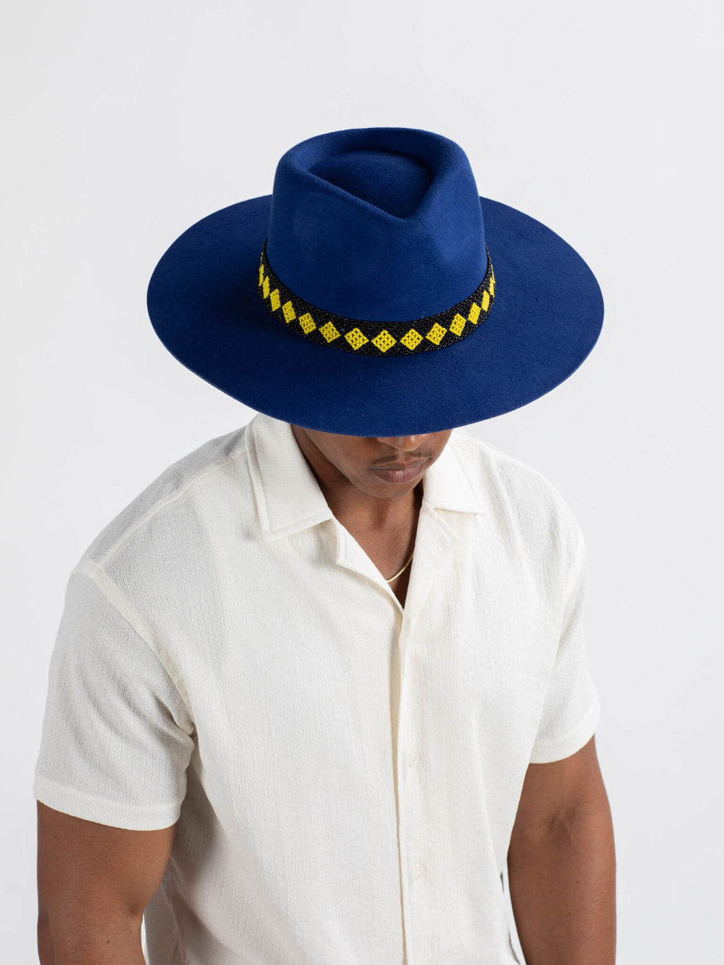 Man wearing The City fedora hat showing  a yellow Rwandan beadwork band. on a white background