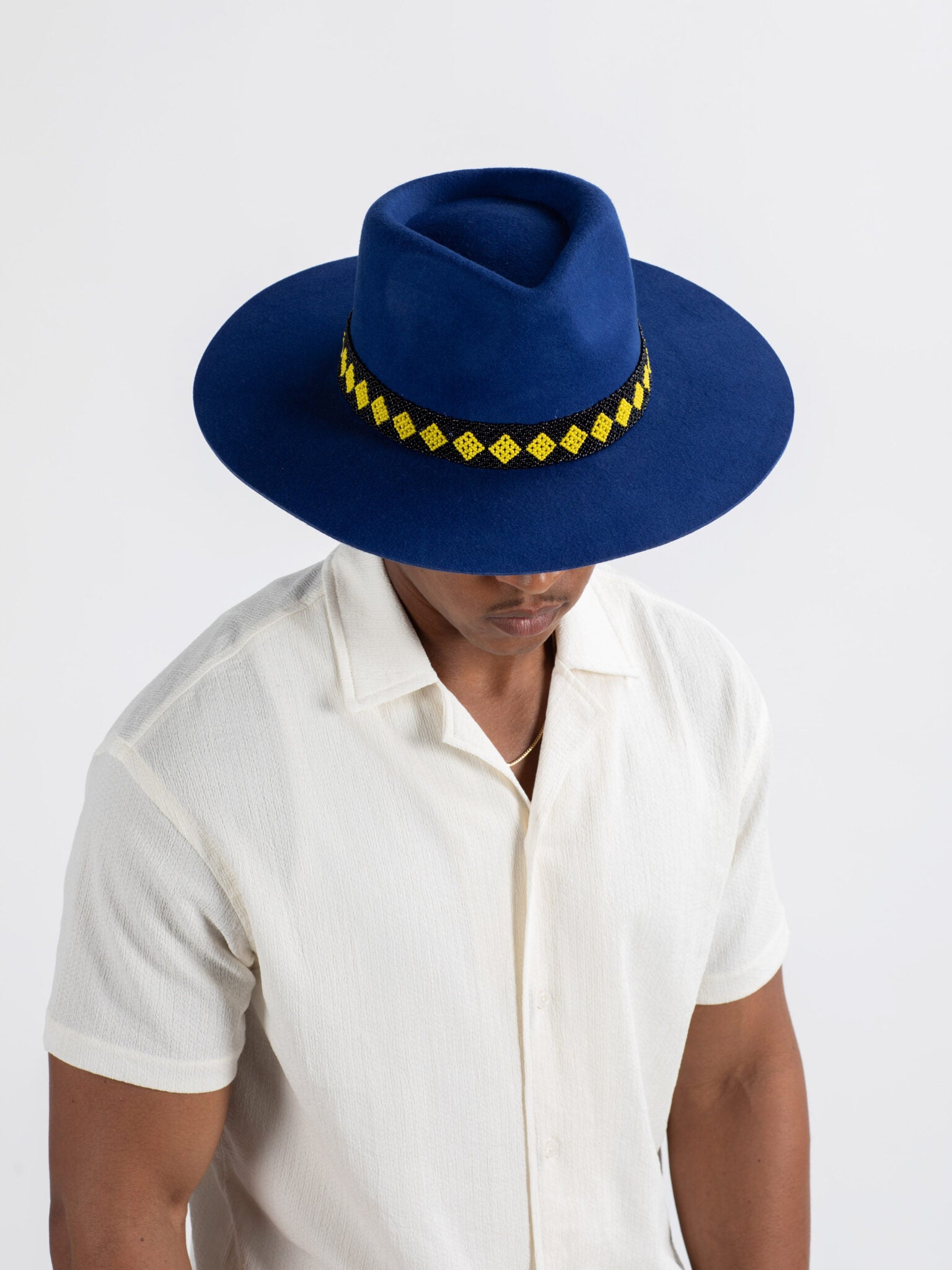 Man wearing The City fedora hat showing  a yellow Rwandan beadwork band. on a white background
